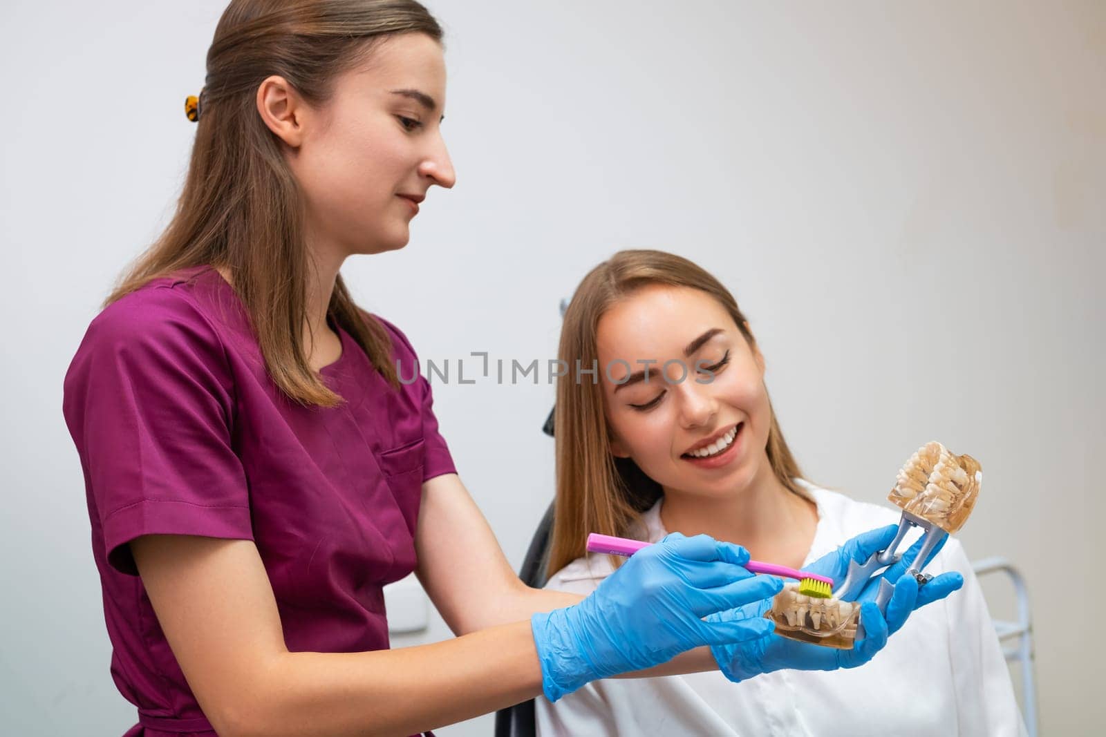 A dental hygienist provides demonstration to woman on the proper technique for cleaning teeth. by vladimka