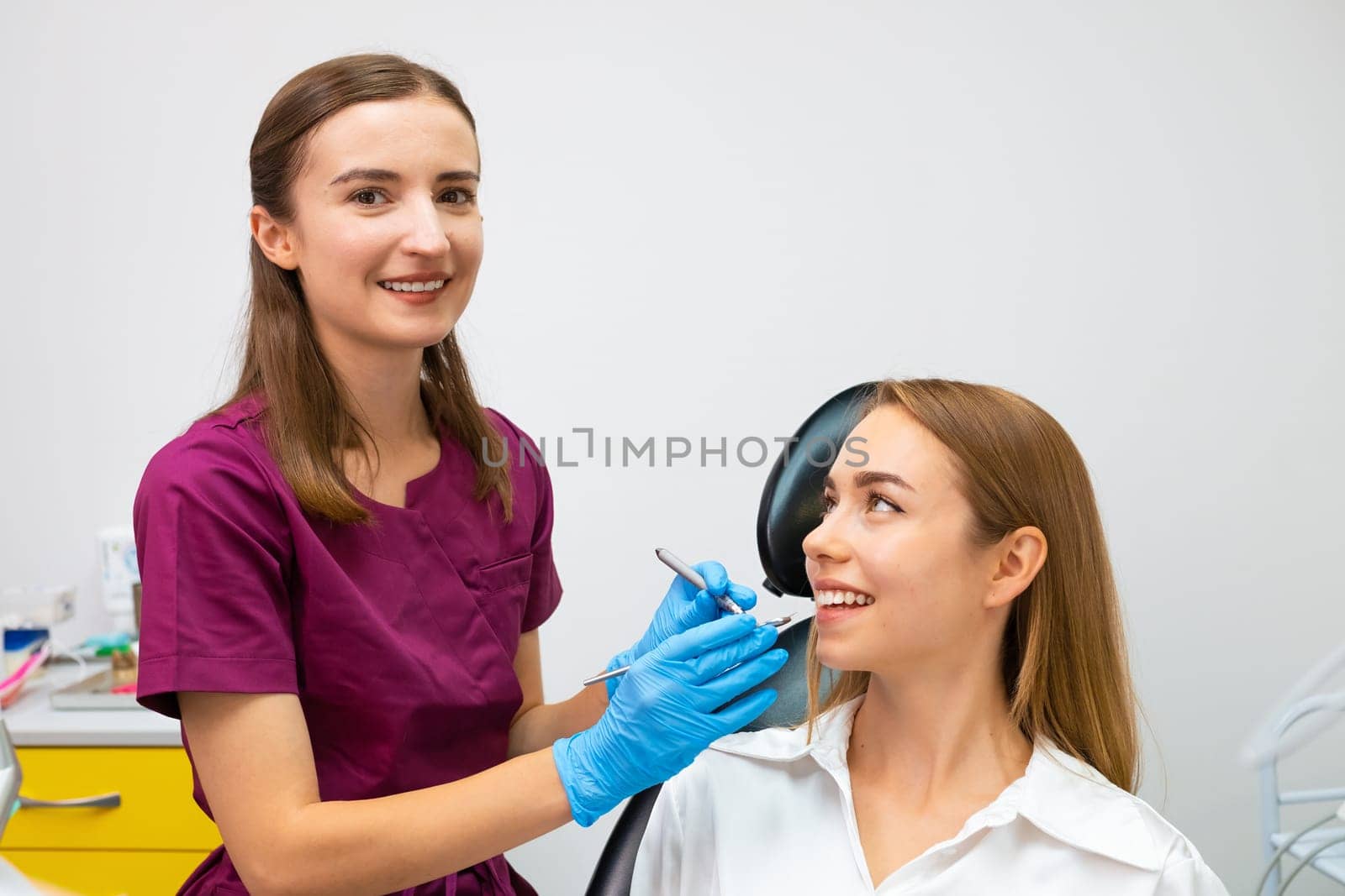 Female orthodontist examining teeth of young patient with perfect smile.