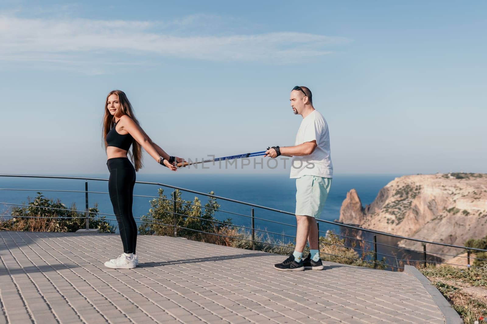 Happy Middle aged couple or friends practicing nordic walking in park near sea. Mature couple with trekking poles walking, practicing Nordic walking outdoors. Aging youthfully and sport concept.