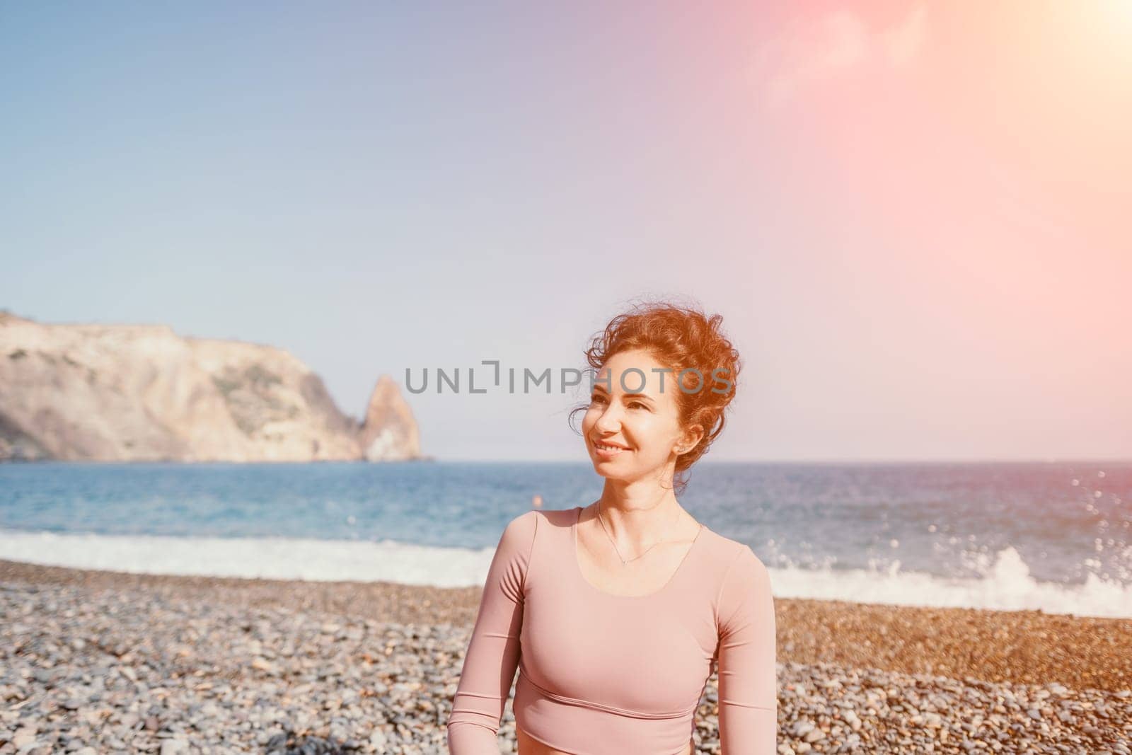 Middle aged well looking woman with black hair doing Pilates with the ring on the yoga mat near the sea on the pebble beach. Female fitness yoga concept. Healthy lifestyle, harmony and meditation.