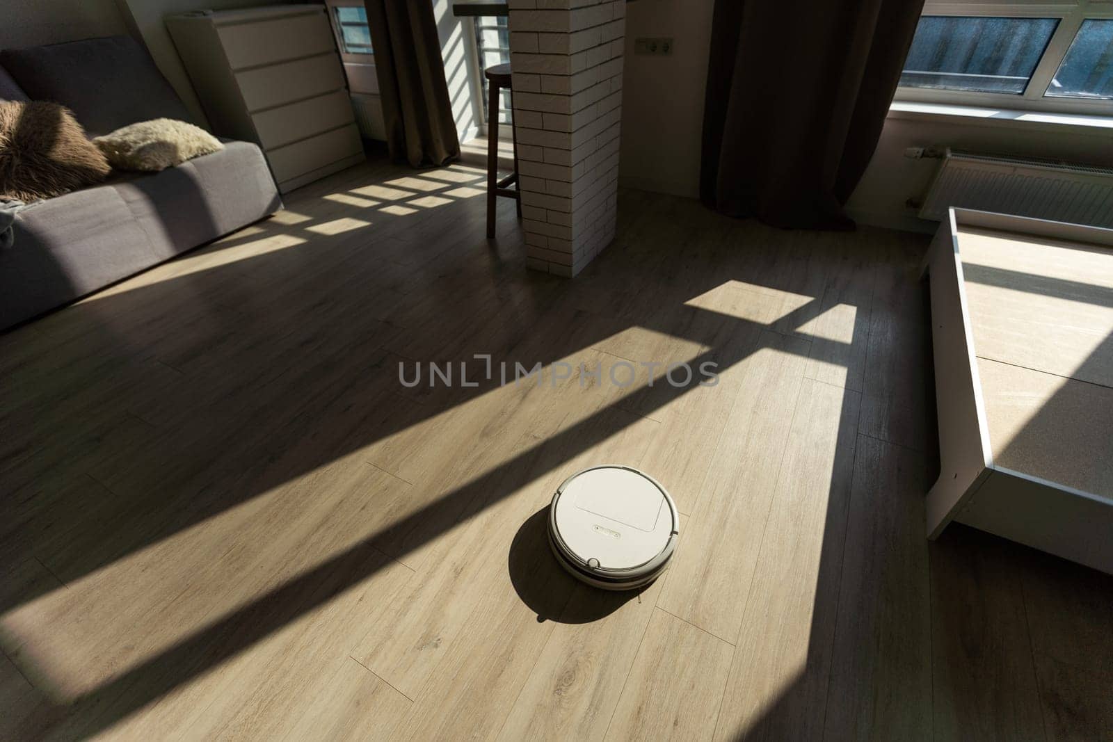 Robot vacuum cleaner on hardwood floor at sunny day.
