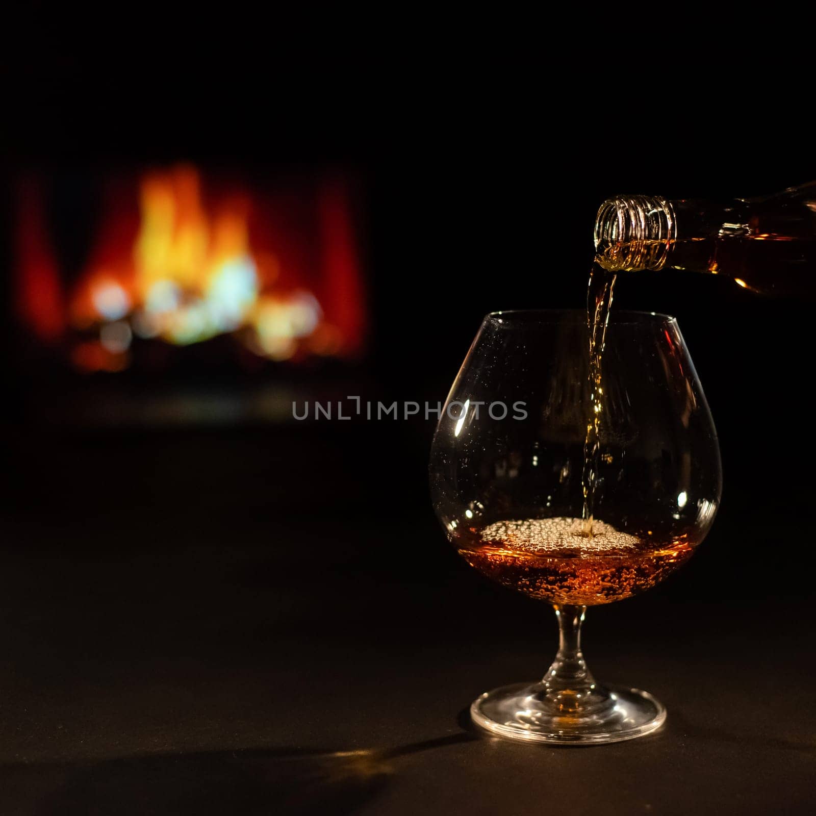 Pour brandy into a glass against the background of the fireplace.