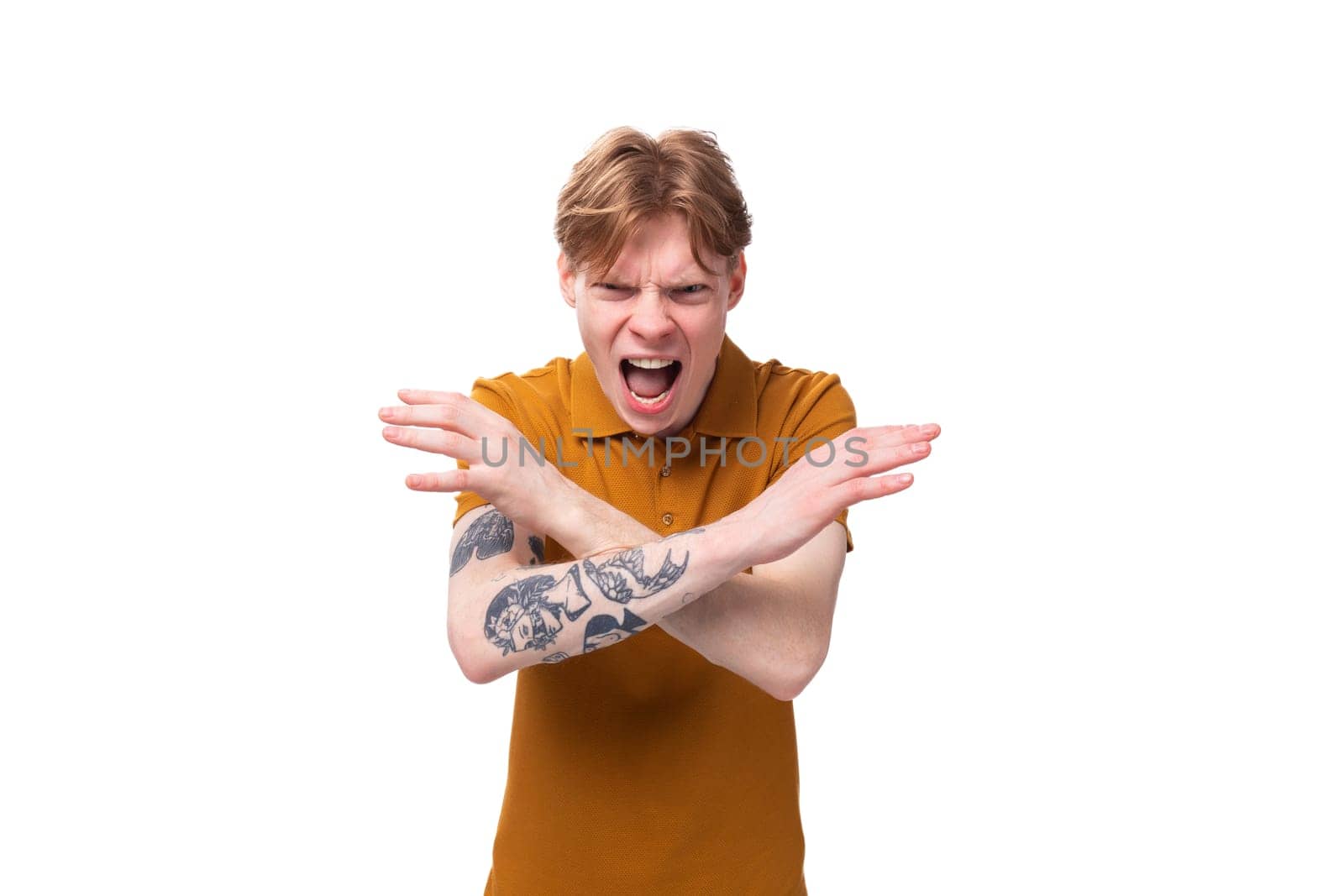 young red-haired caucasian male student with a tattoo dressed in an orange t-shirt feels angry and screams.