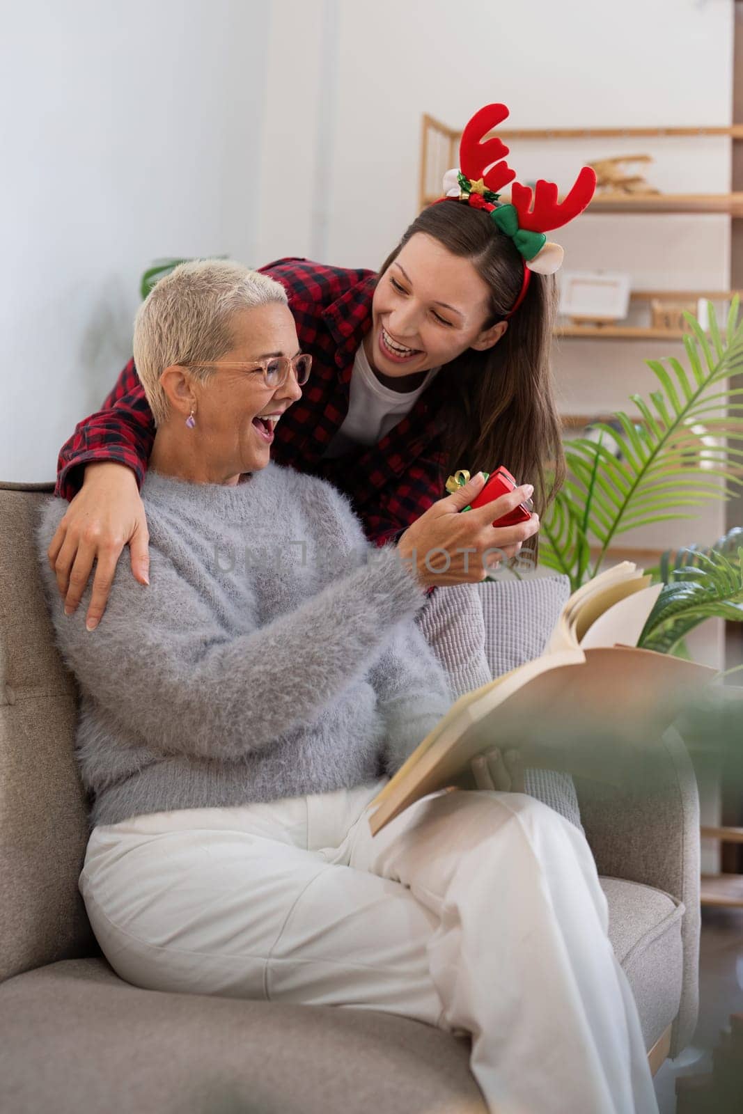 Merry Christmas senior woman with adult daughter exchange gift home.