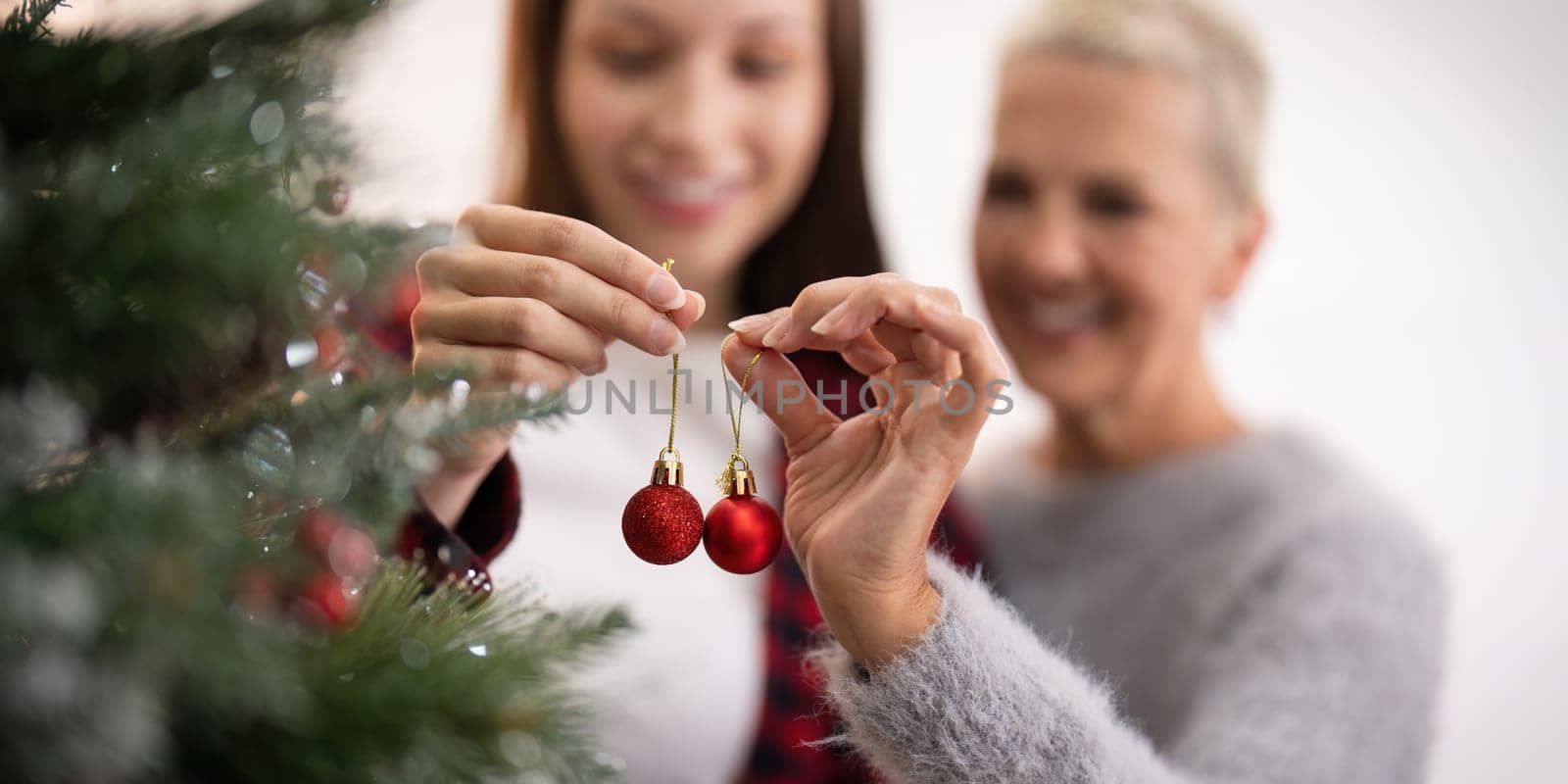 Family winter holiday and concept happy senior woman with adult daughter decorate christmas tree at home by nateemee