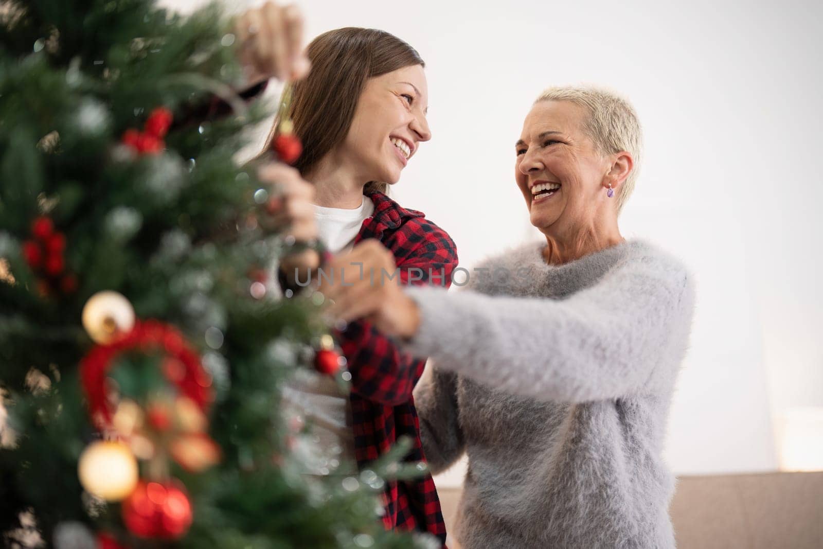 Family winter holiday and concept happy senior woman with adult daughter decorate christmas tree at home by nateemee