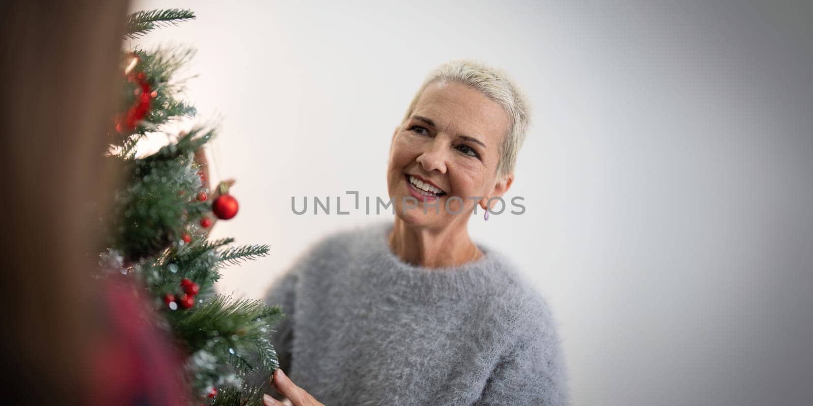 Cheerful elderly woman decorat the christmas tree. Christmas atmosphere at cozy home interior.