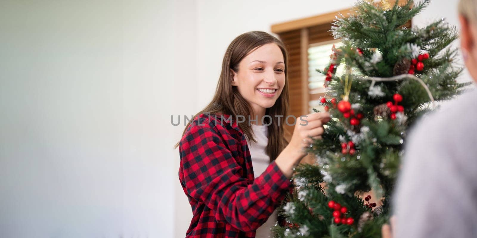 Happy senior woman with adult daughter decorate christmas tree at home.