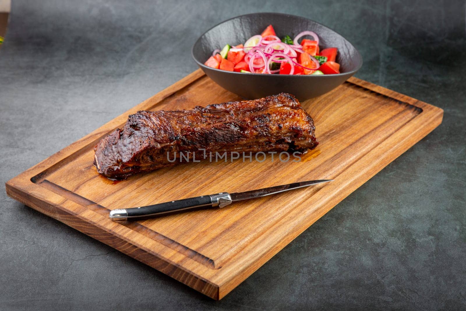 well-done steak with tomato and cucumber salad on a wooden tray