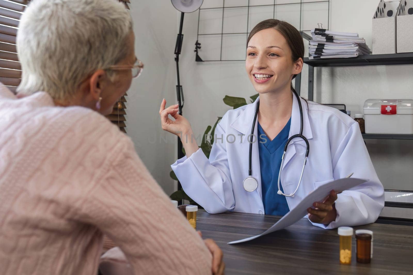 Female doctor in white coat talking with elderly patient in clinic, giving advice on health and health care and medication, medicine concept by wichayada