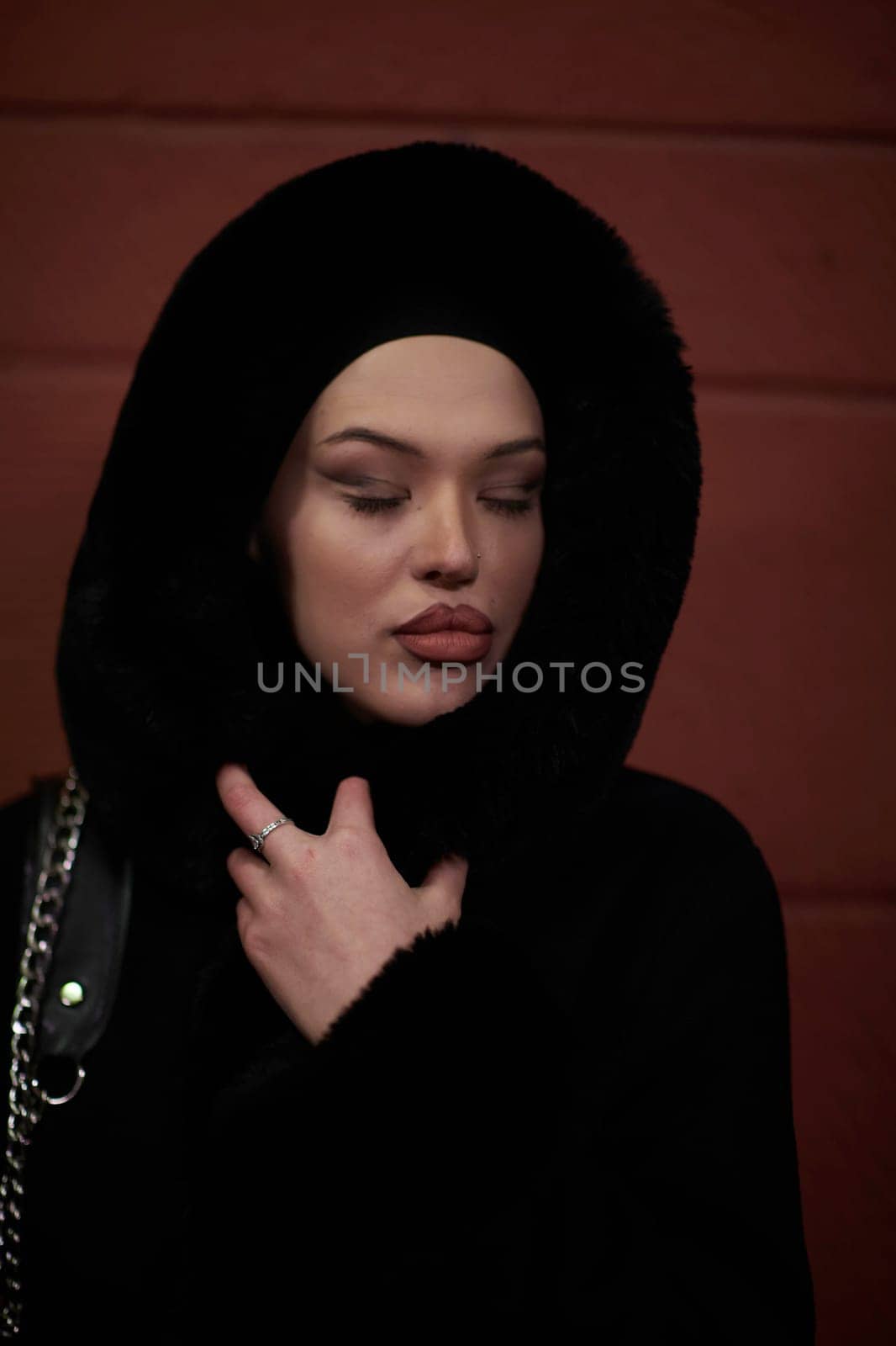 Young Muslim woman walking on urban city street on a cold winter night wearing hijab scarf veil a fashionable coat with bokeh city light in the background.