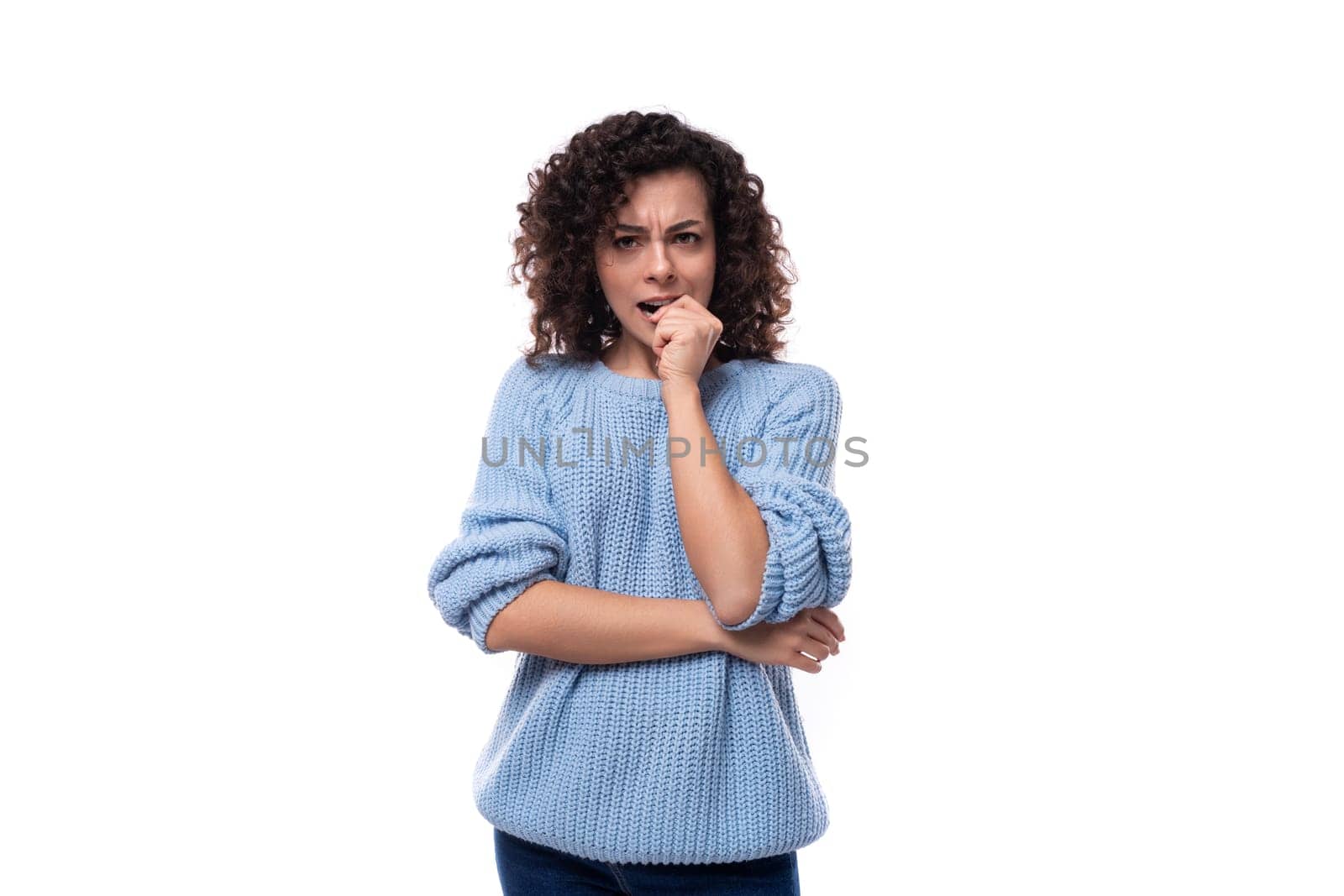 a young brunette woman with curls is dressed in a blue knitted sweater is brainstorming.