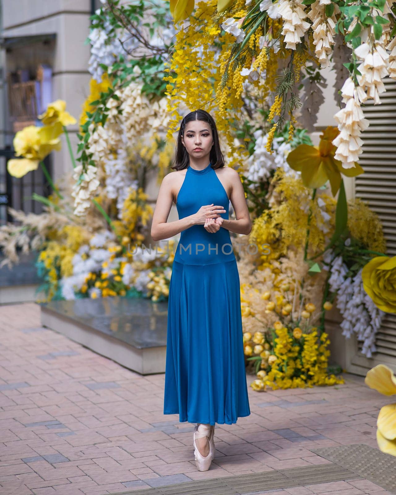 Beautiful Asian ballerina posing against the backdrop of a building decorated with flowers