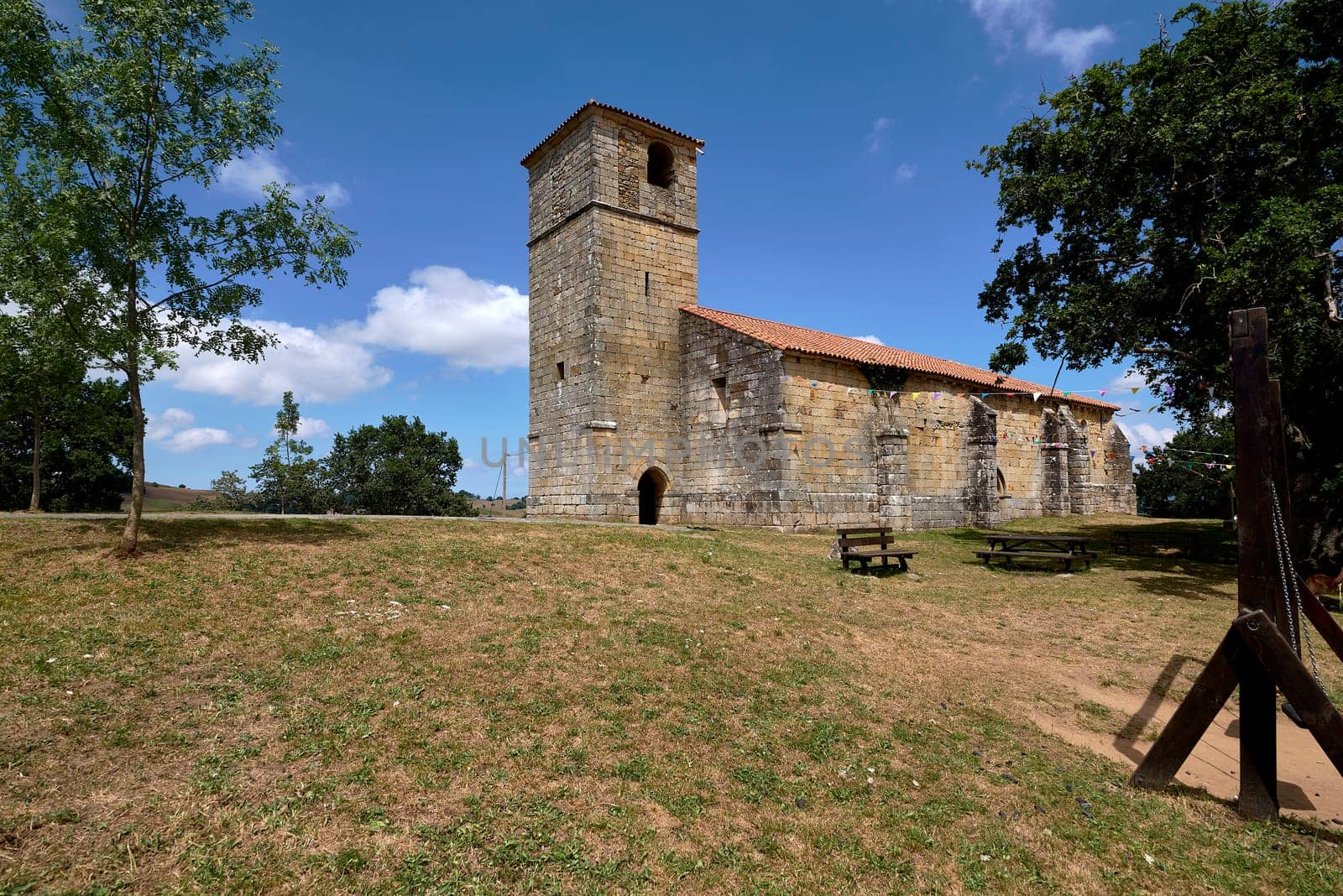 Church of San Pantaleon or San Sebastian in Lierganes on a bright summer day.Romanesque, tower, masonry, stone, vegetation, light, luminous, blue sky with clouds
