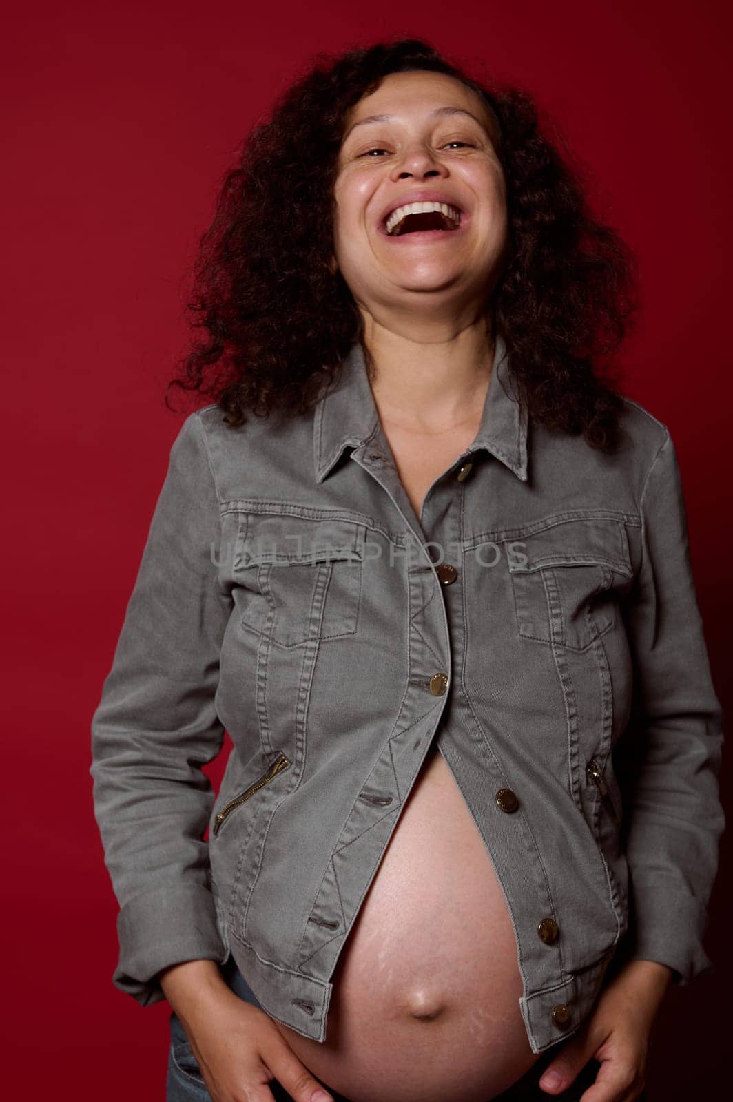 Happy pregnant woman with naked belly, wearing stylish casual denim blazer and jeans, laughing looking at camera by artgf