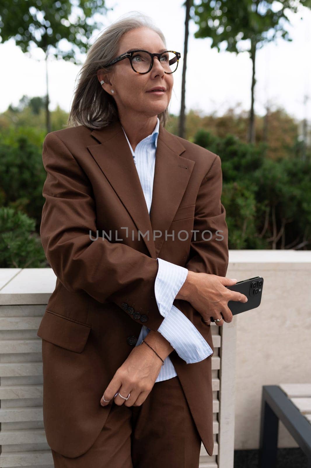 well-groomed business woman of mature years dressed in an elegant brown suit walks around the city.