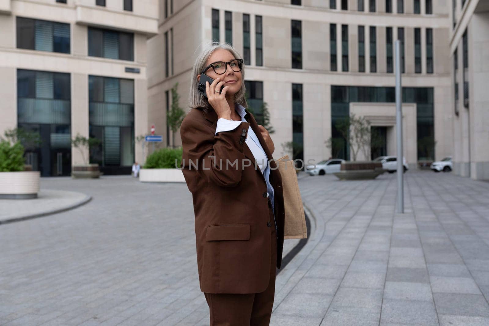 pretty gray-haired retired woman dressed in an elegant suit talking on the phone while walking down the street.