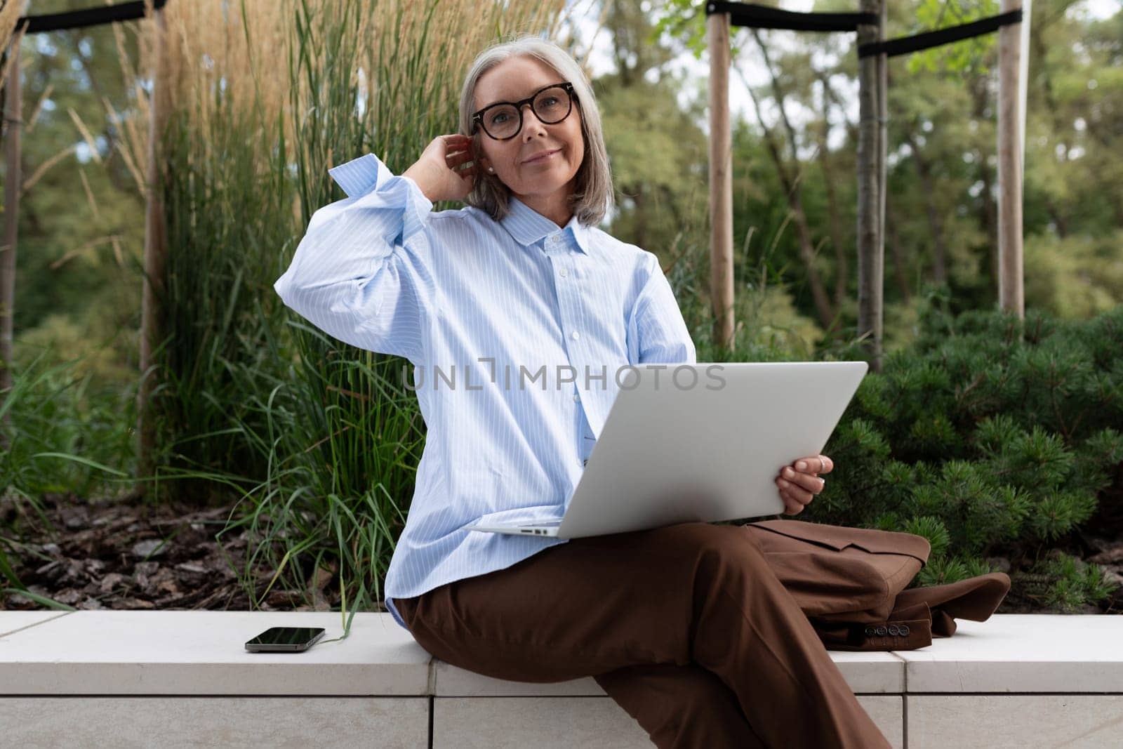 close-up of a slender well-groomed pretty gray-haired business woman pensioner against the background of greenery.