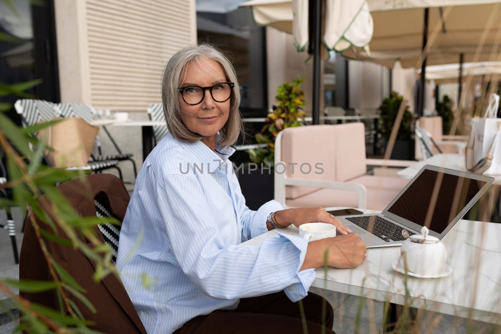 slender cute gray-haired entrepreneur woman of mature years in a light shirt is resting during a break by TRMK