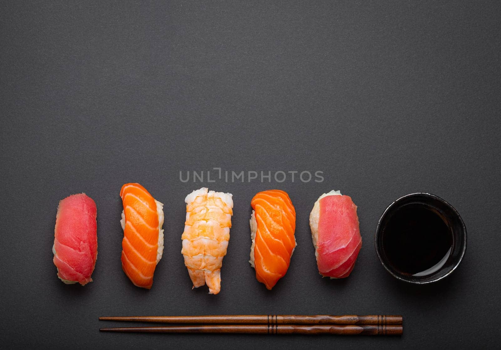 Traditional Japanese sushi top view with soy sauce and chopsticks on dark black minimal background. Sushi with salmon, tuna and shrimp, space for text
