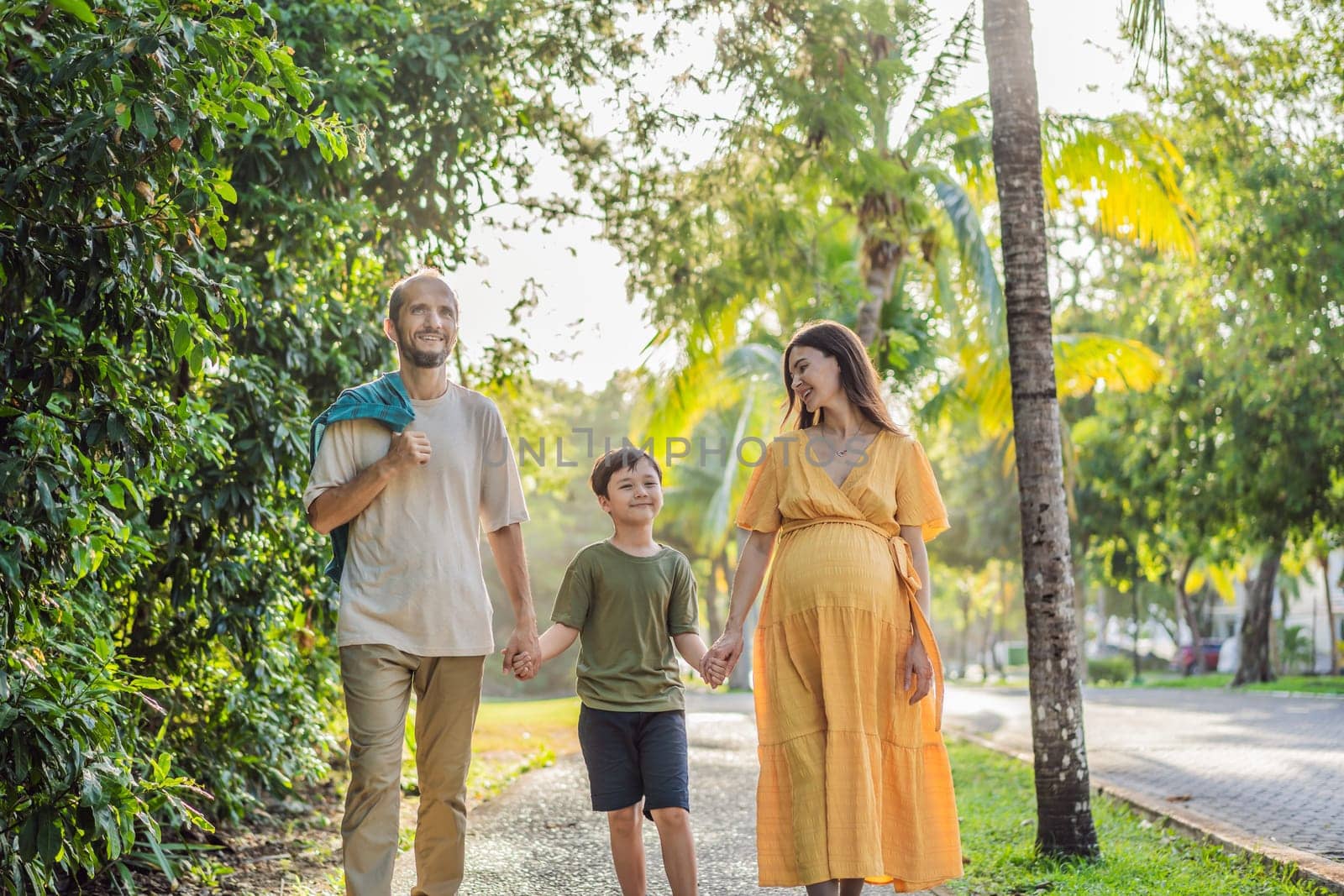 A loving family enjoying a leisurely walk in the park - a radiant pregnant woman after 40, embraced by her husband, and accompanied by their adult teenage son, savoring precious moments together amidst nature's beauty. Pregnancy after 40 concept by galitskaya