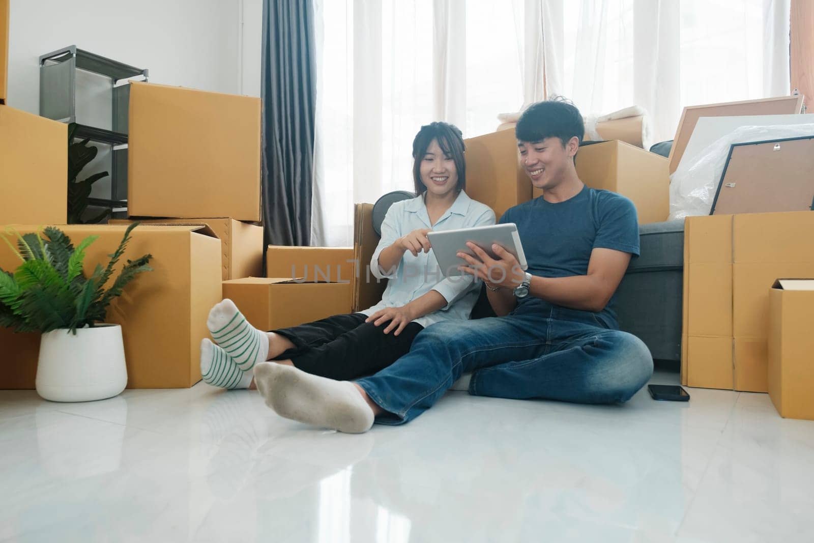 Happy couple sitting and rest with cardboard boxes in new house at moving day. New house owner and real estate concept.