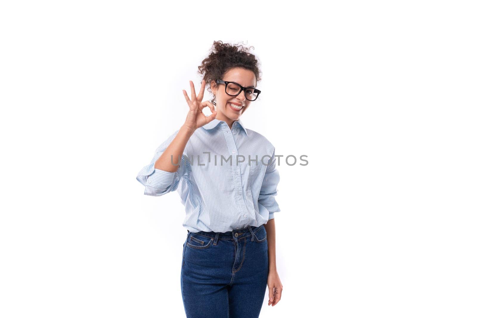 beautiful young stylish caucasian office worker woman with curly hair wears glasses for image and light blue shirt.