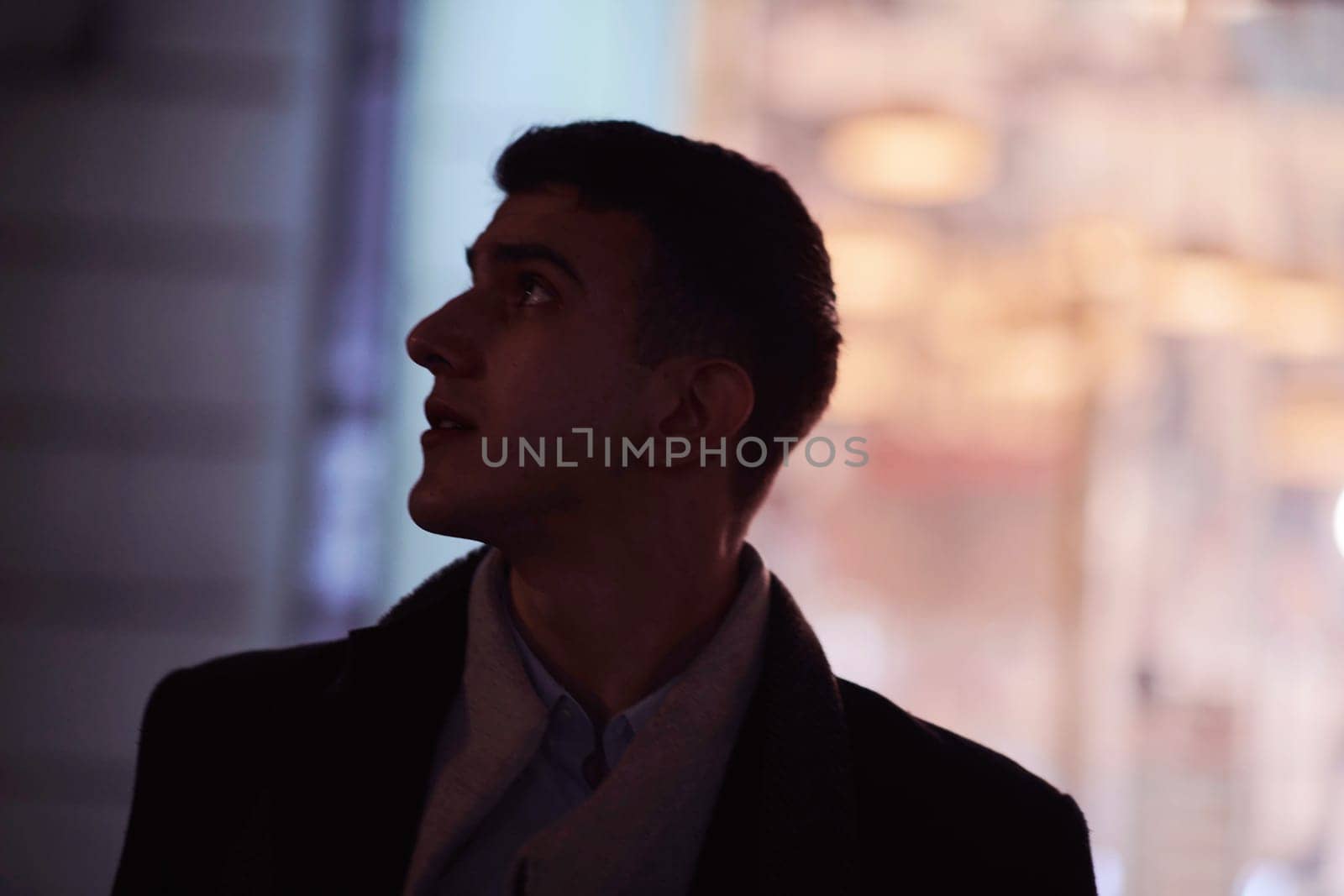 Smiling Meedle Eastern man walking down street near modern office building, freelancer businessman looking away holding mobile phone on busy city street at night