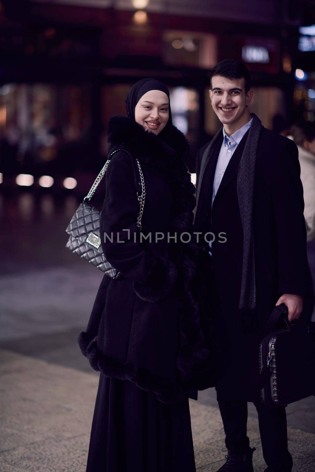 Happy multicultural business couple walking together outdoors in an urban city street at night near a jewelry shopping store window. by dotshock