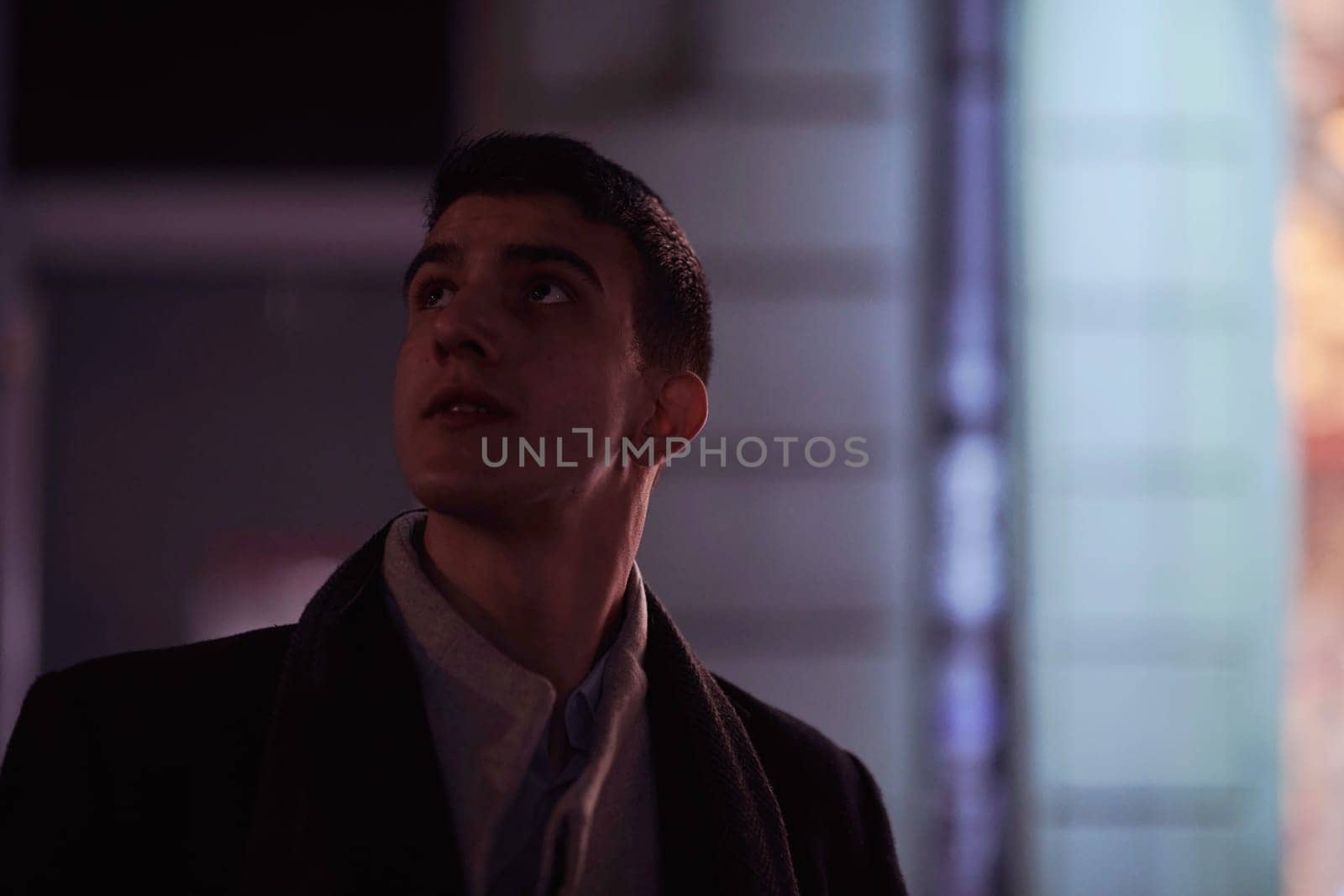 Smiling Meedle Eastern man walking down street near modern office building, freelancer businessman looking away holding mobile phone on busy city street at night