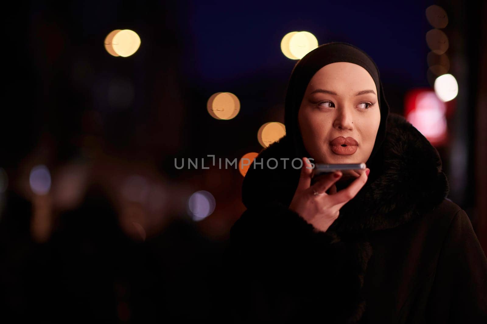 Beautiful and elegant European Muslim Hijabi Business Lady checking her phone and social media on urban city street at night