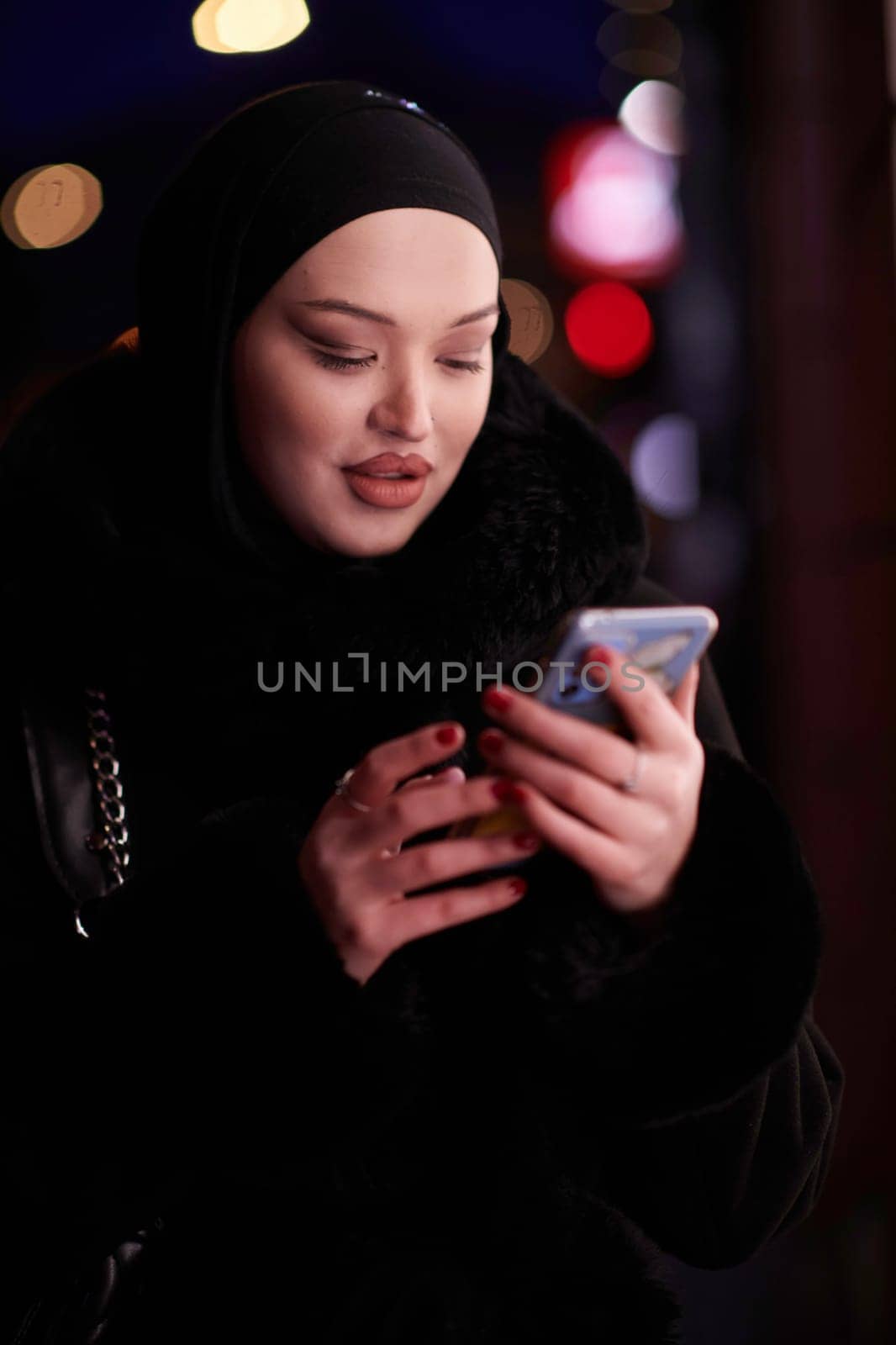 uropean Muslim Hijabi Business Lady checking her phone on urban city street at night by dotshock