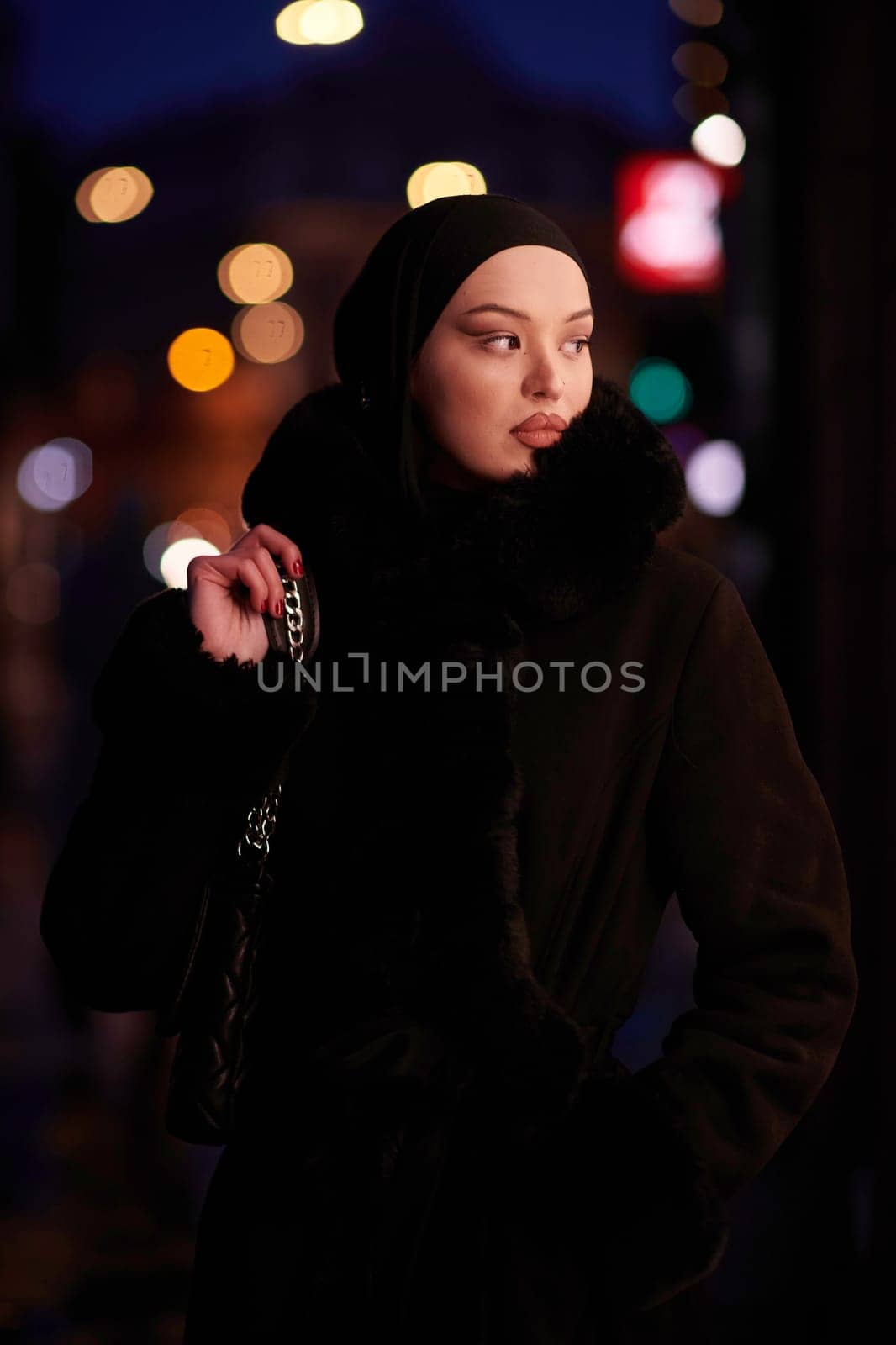 Muslim woman walking on an urban city street on a cold winter night wearing hijab by dotshock