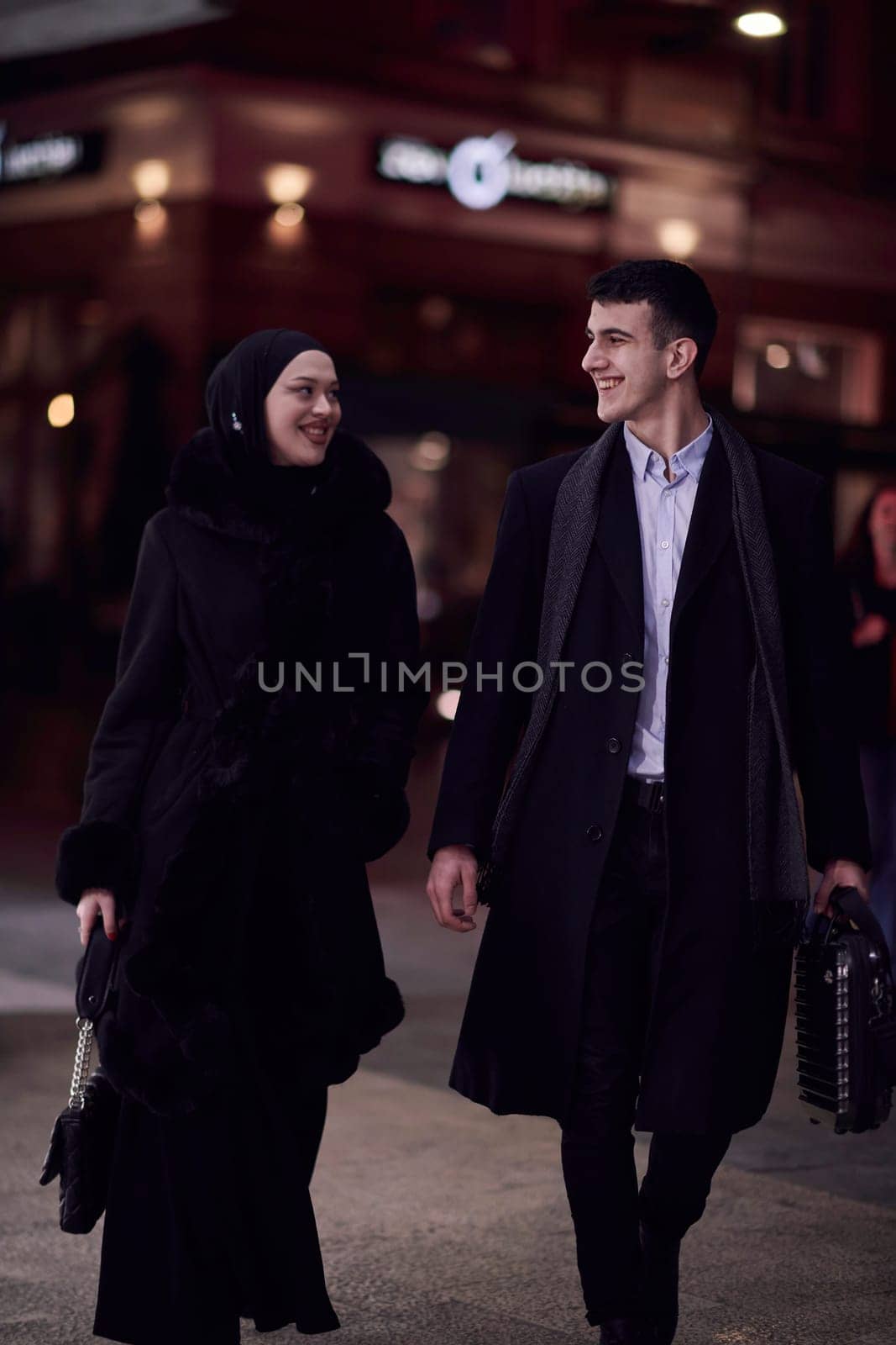 Happy multicultural business couple walking together outdoors in an urban city street at night near a jewelry shopping store window. by dotshock