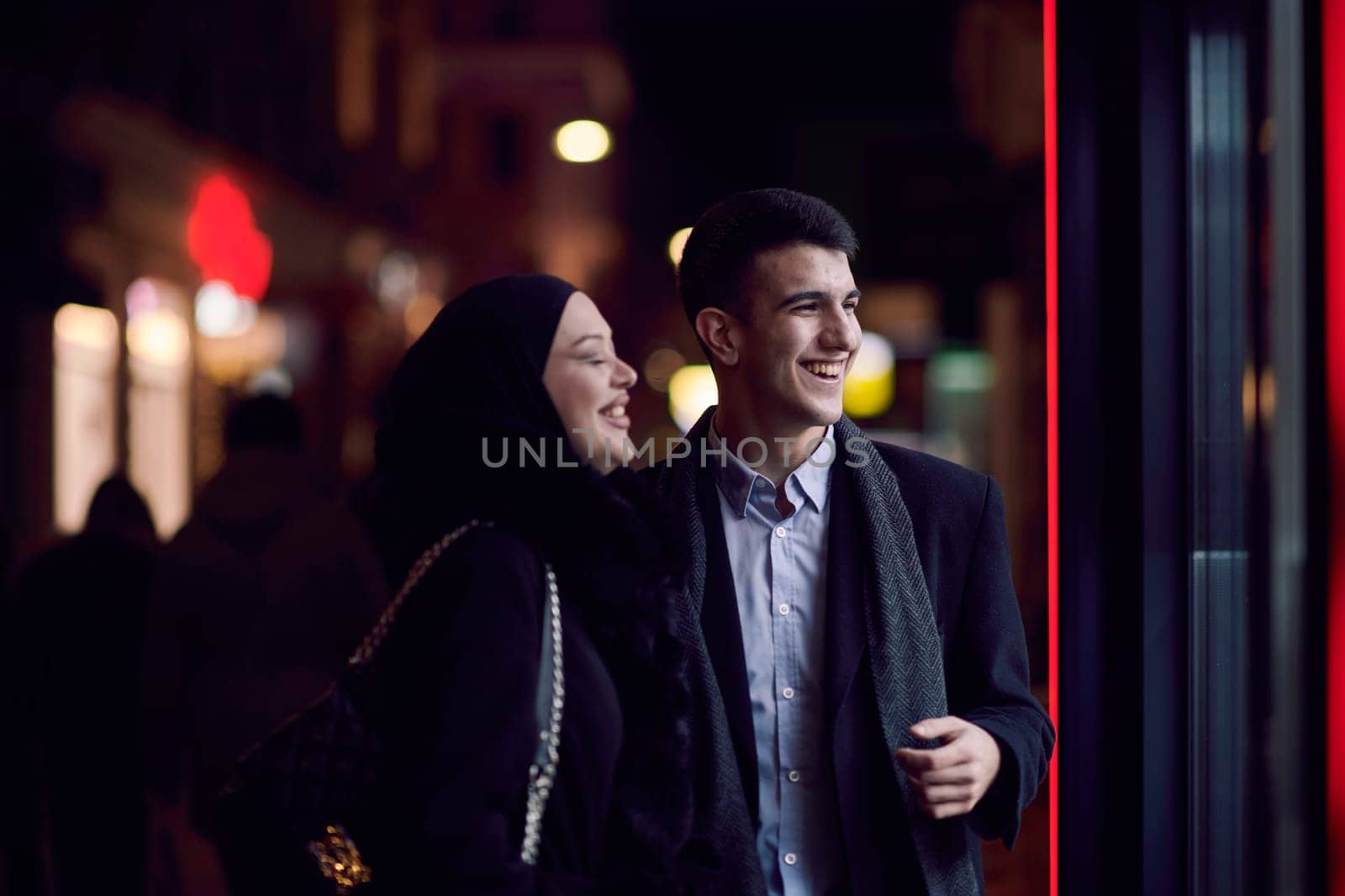 Happy multicultural business couple walking together outdoors in an urban city street at night near a jewelry shopping store window. by dotshock