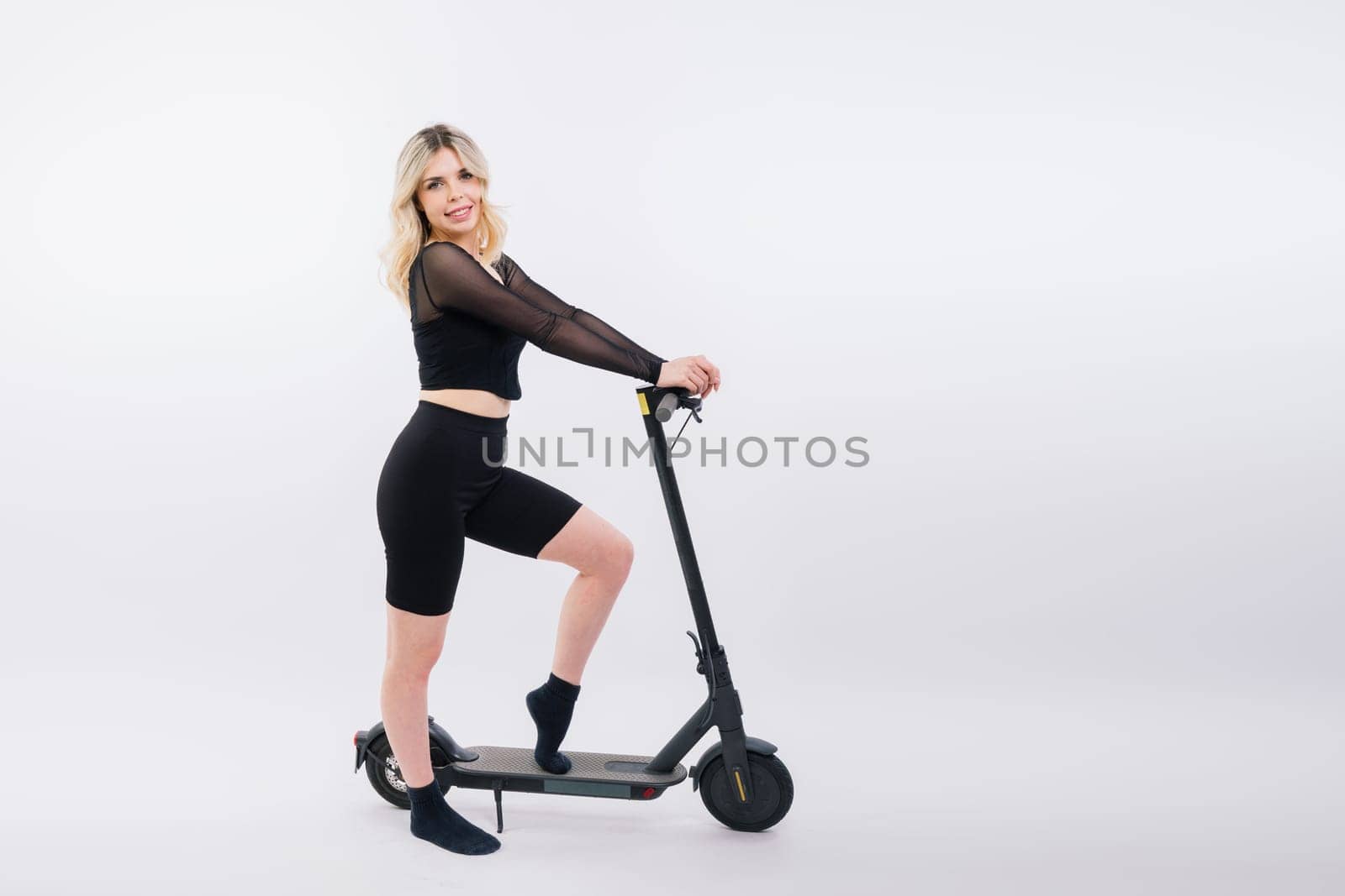 Beautiful emotional young female in a sport clothes on electric scooter on red and white background