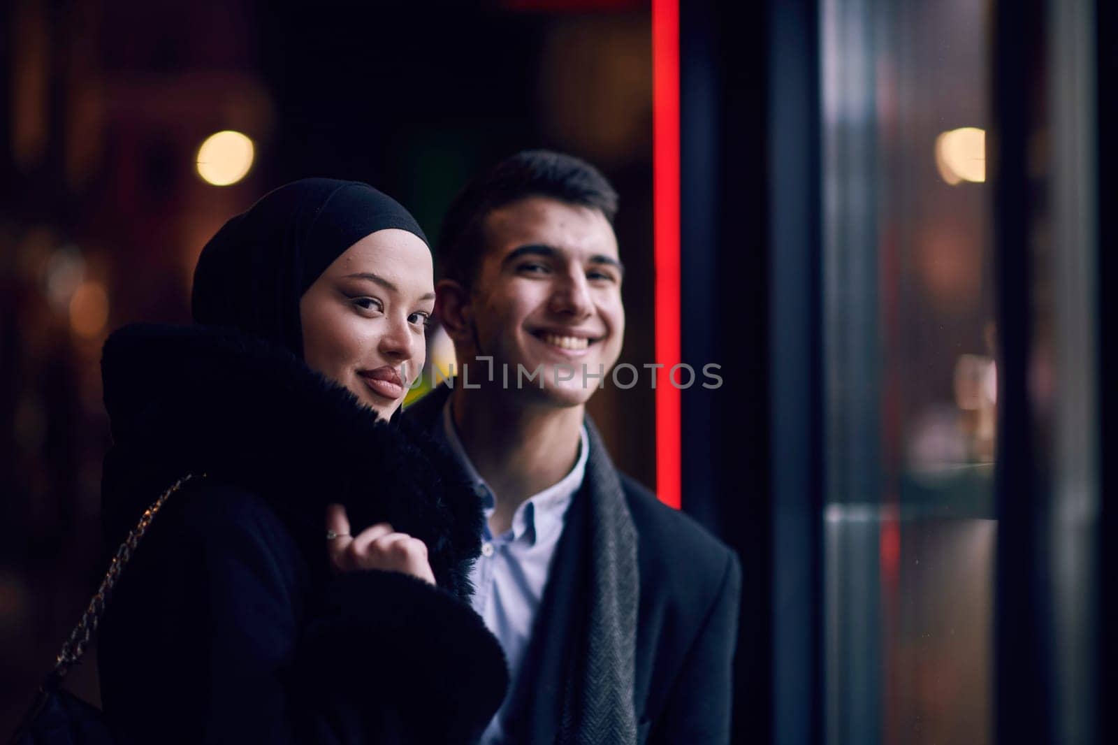 Happy multicultural business couple walking together outdoors in an urban city street at night near a jewelry shopping store window. by dotshock