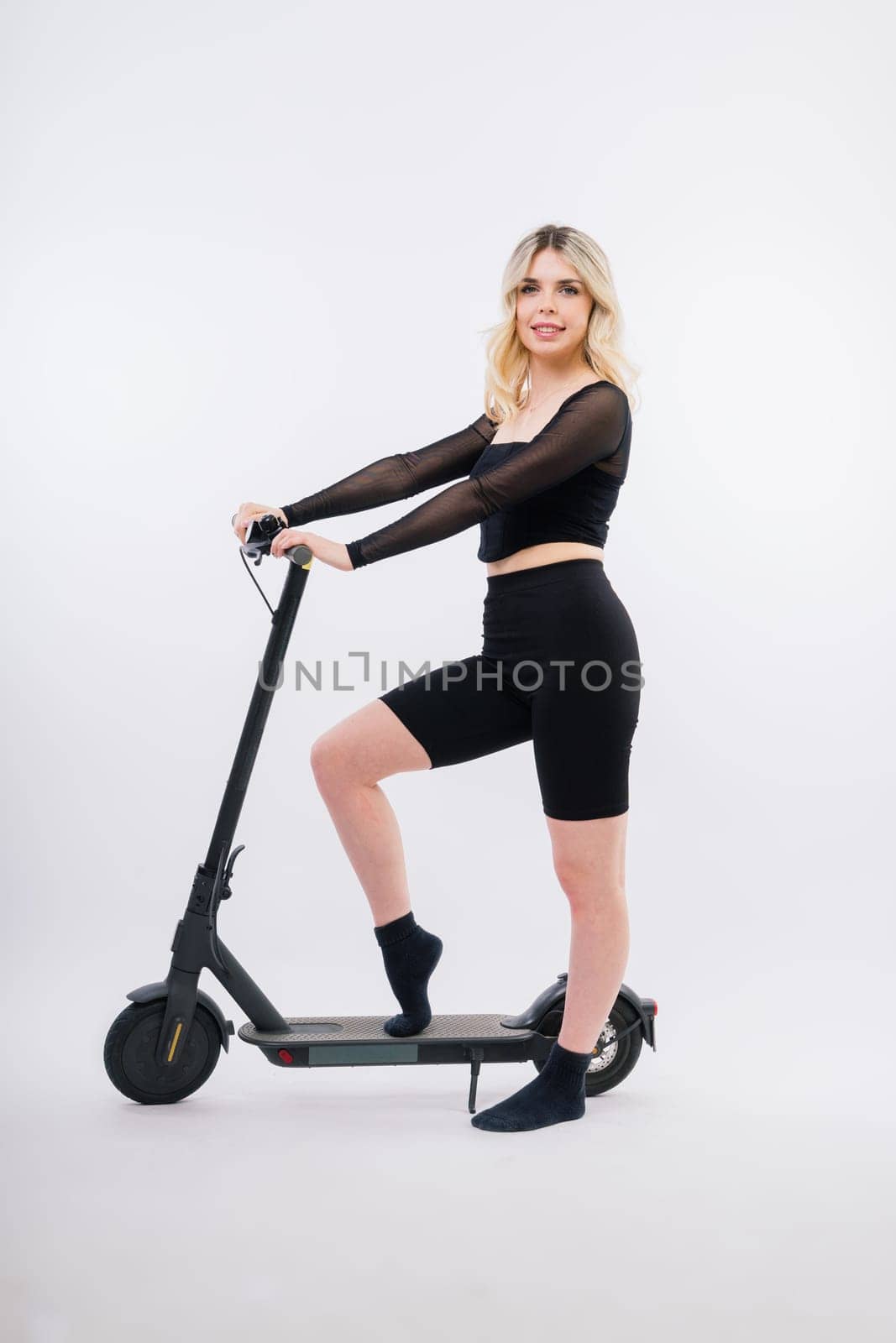 Beautiful emotional young female in sport clothes on electric scooter on red and white background by Zelenin