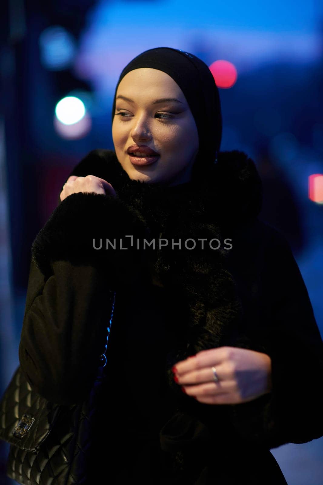 Muslim woman walking on an urban city street on a cold winter night wearing hijab with bokeh city lights in the background