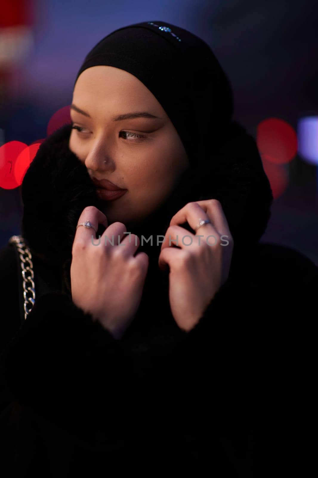 Muslim woman walking on an urban city street on a cold winter night wearing hijab with bokeh city lights in the background