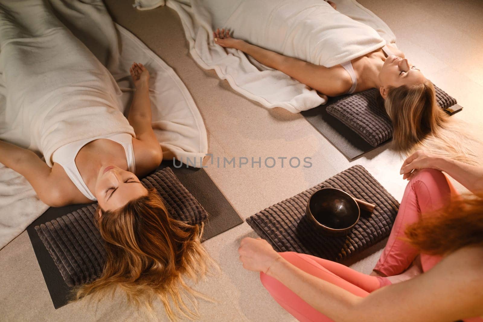 girls lying on the floor relax to the sounds of a Tibetan bowl in the fitness room by Lobachad