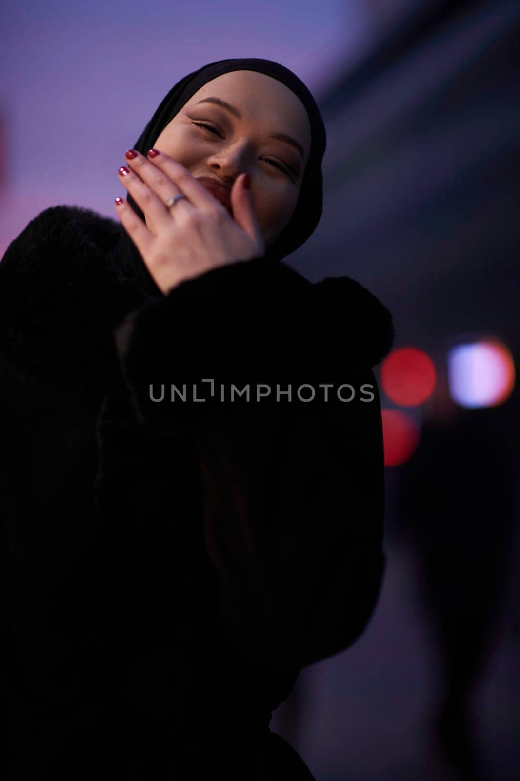 Muslim woman walking on an urban city street on a cold winter night wearing hijab with bokeh city lights in the background