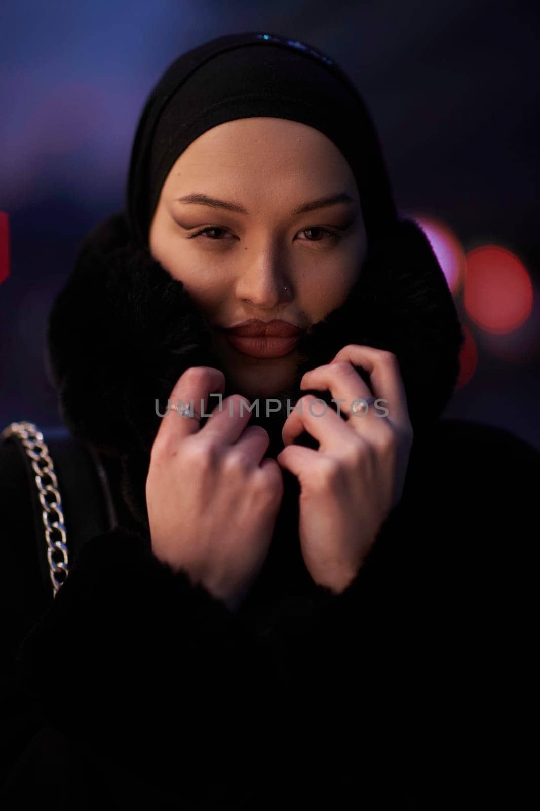 Muslim woman walking on an urban city street on a cold winter night wearing hijab with bokeh city lights in the background