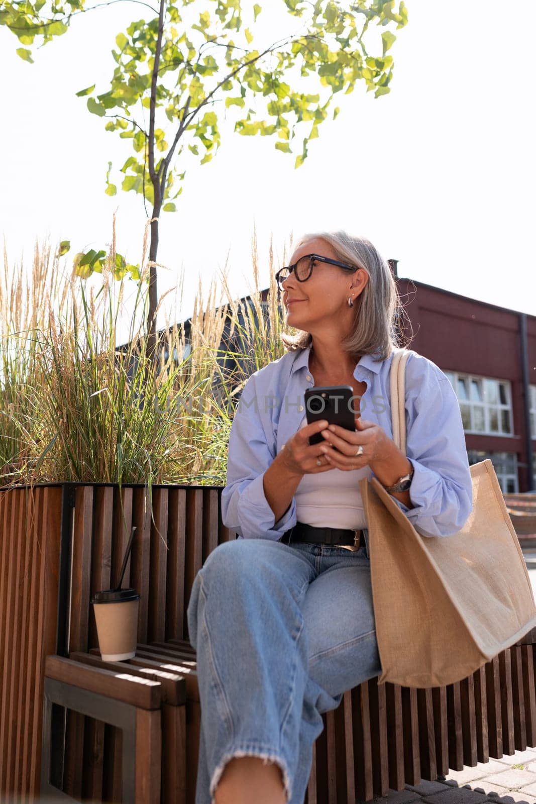 a well-groomed middle-aged woman with a bob haircut enjoys summer sitting on a bench and waiting for a partner.