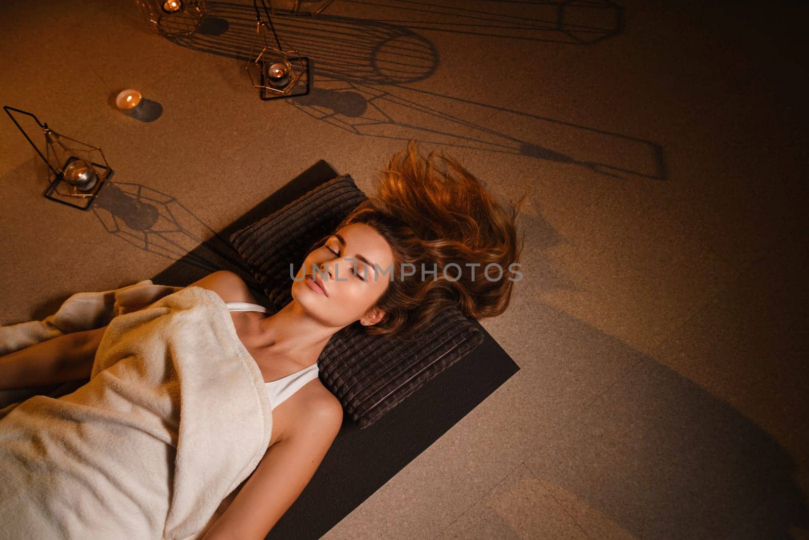 A woman lies on the floor covered with a blanket with her eyes closed and relaxes after a workout , shavasana pose.