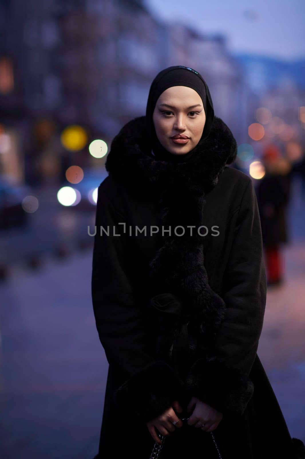 Muslim woman walking on an urban city street on a cold winter night wearing hijab with bokeh city lights in the background