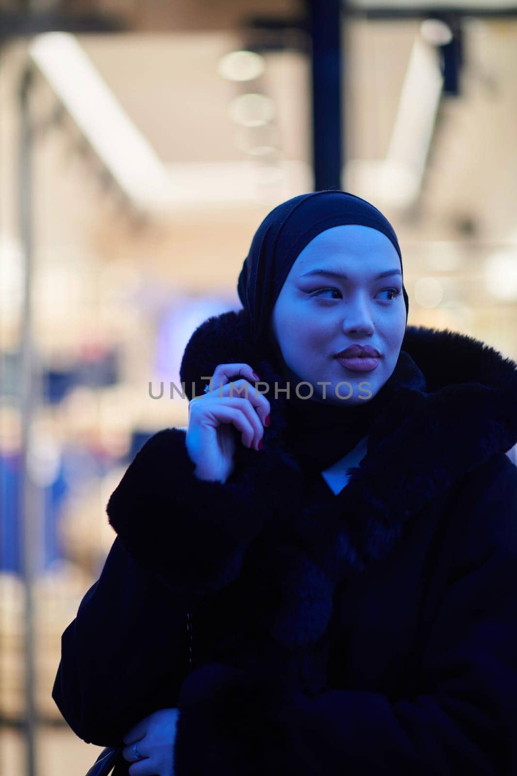 Muslim woman walking on an urban city street on a cold winter night wearing hijab with bokeh city lights in the background