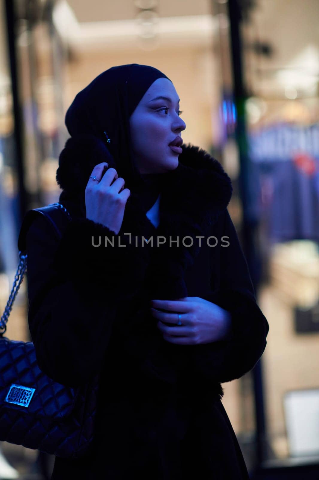 Muslim woman walking on an urban city street on a cold winter night wearing hijab with bokeh city lights in the background