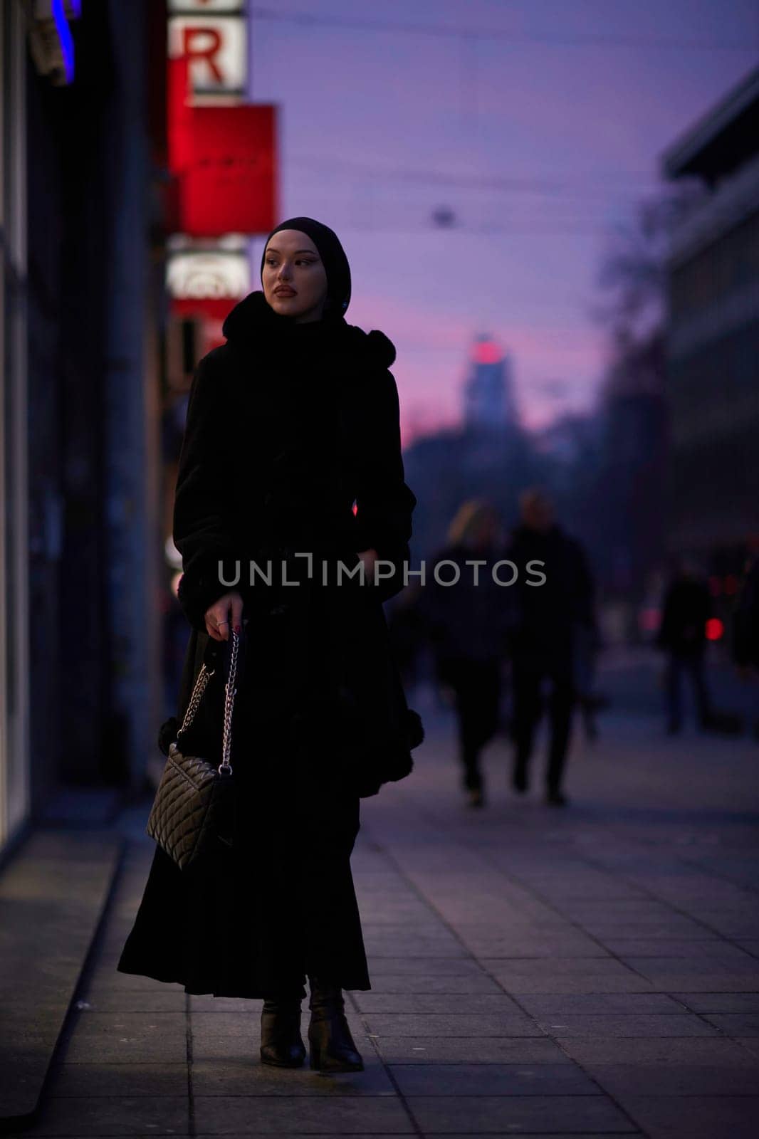 Muslim woman walking on an urban city street on a cold winter night wearing hijab by dotshock