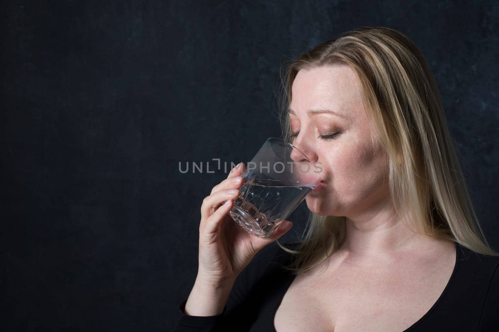 portrait caucasian middel aged woman in black blouse drinking water in the dark room,healthy lifstile concept,best detox drink,elastic skin, strong hair and nails,energy and vigor,High quality photo